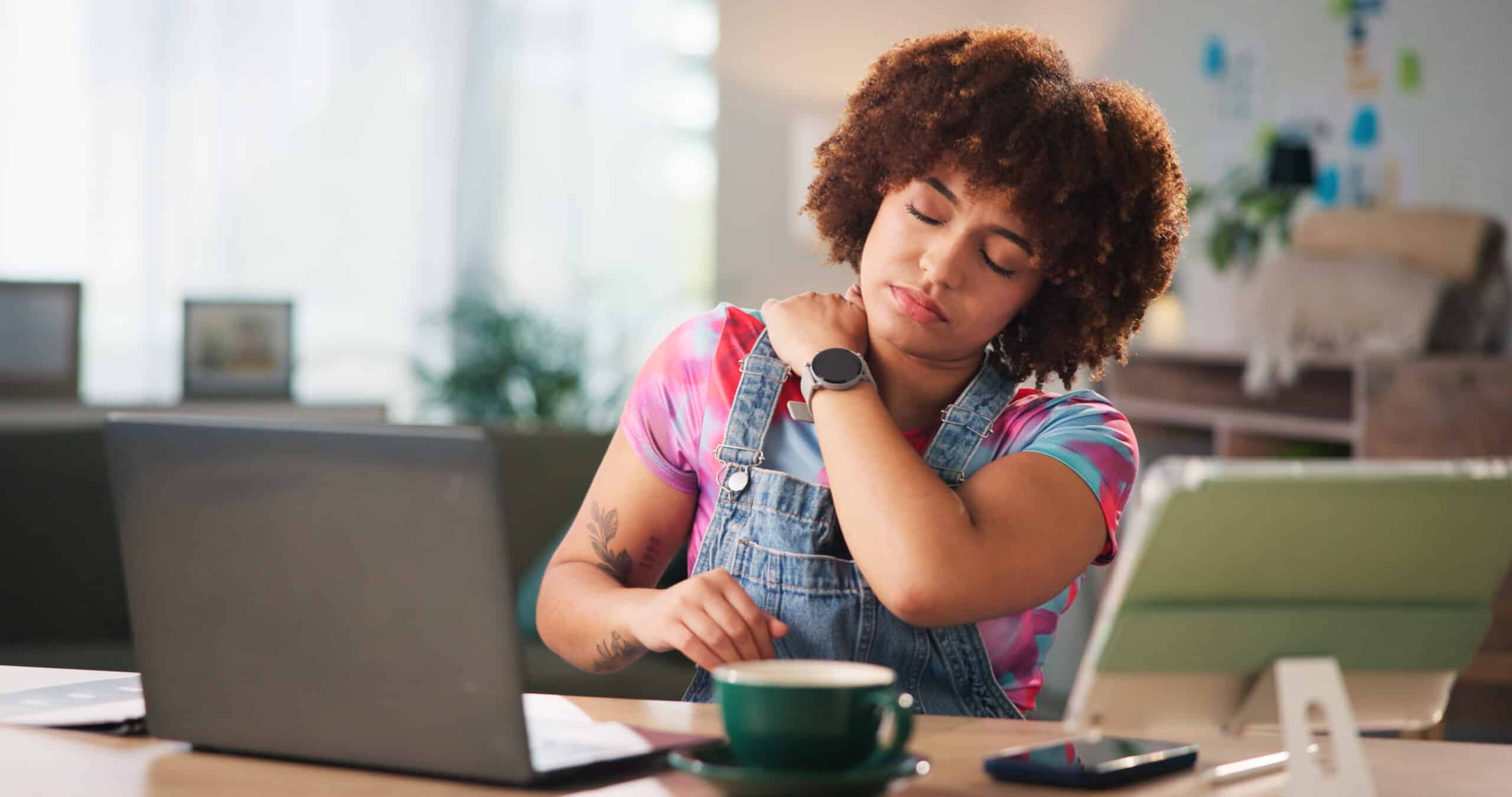 woman holding her neck in pain in front of a laptop